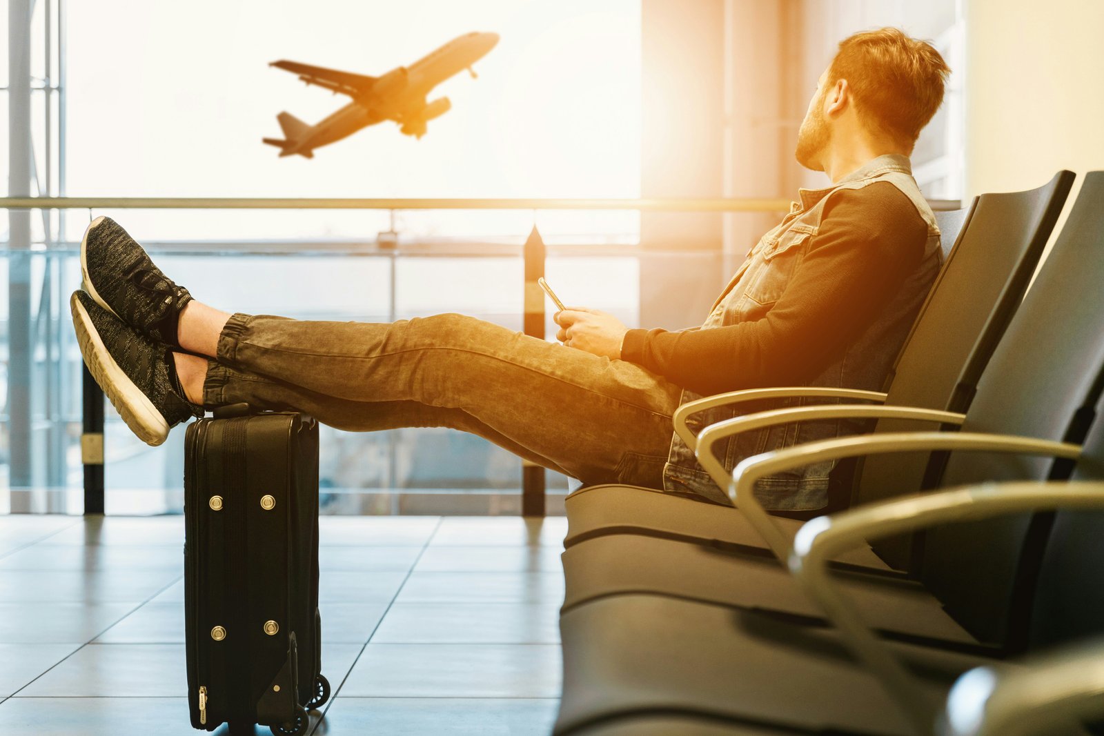 Viaggiatore in attesa in aeroporto, valigia pronta accanto a sé